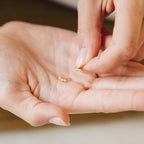 A person holding Stella Star Studs—delicate gold earrings adorned with small stones—in the palm of their hand.