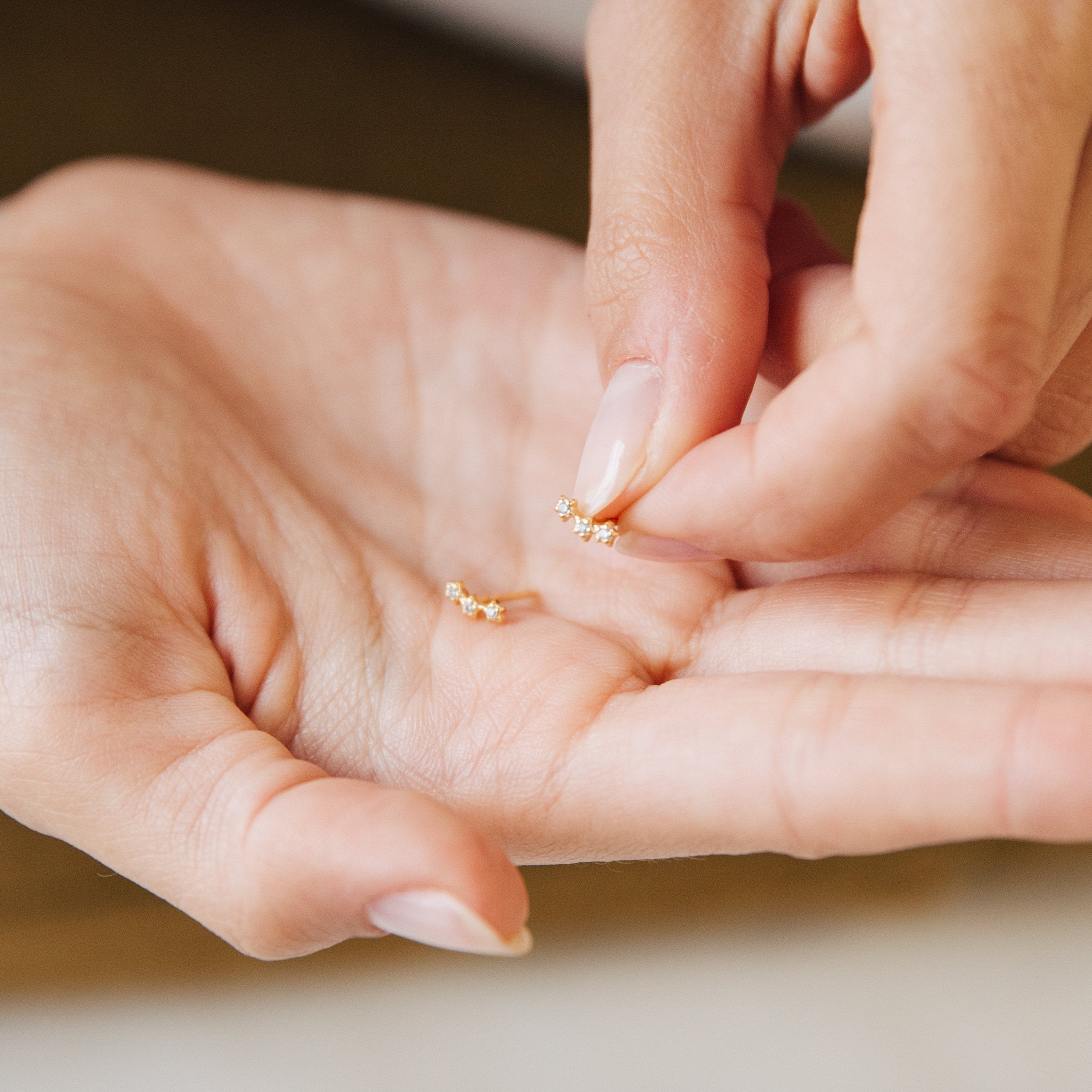 A person holding Stella Star Studs—delicate gold earrings adorned with small stones—in the palm of their hand.