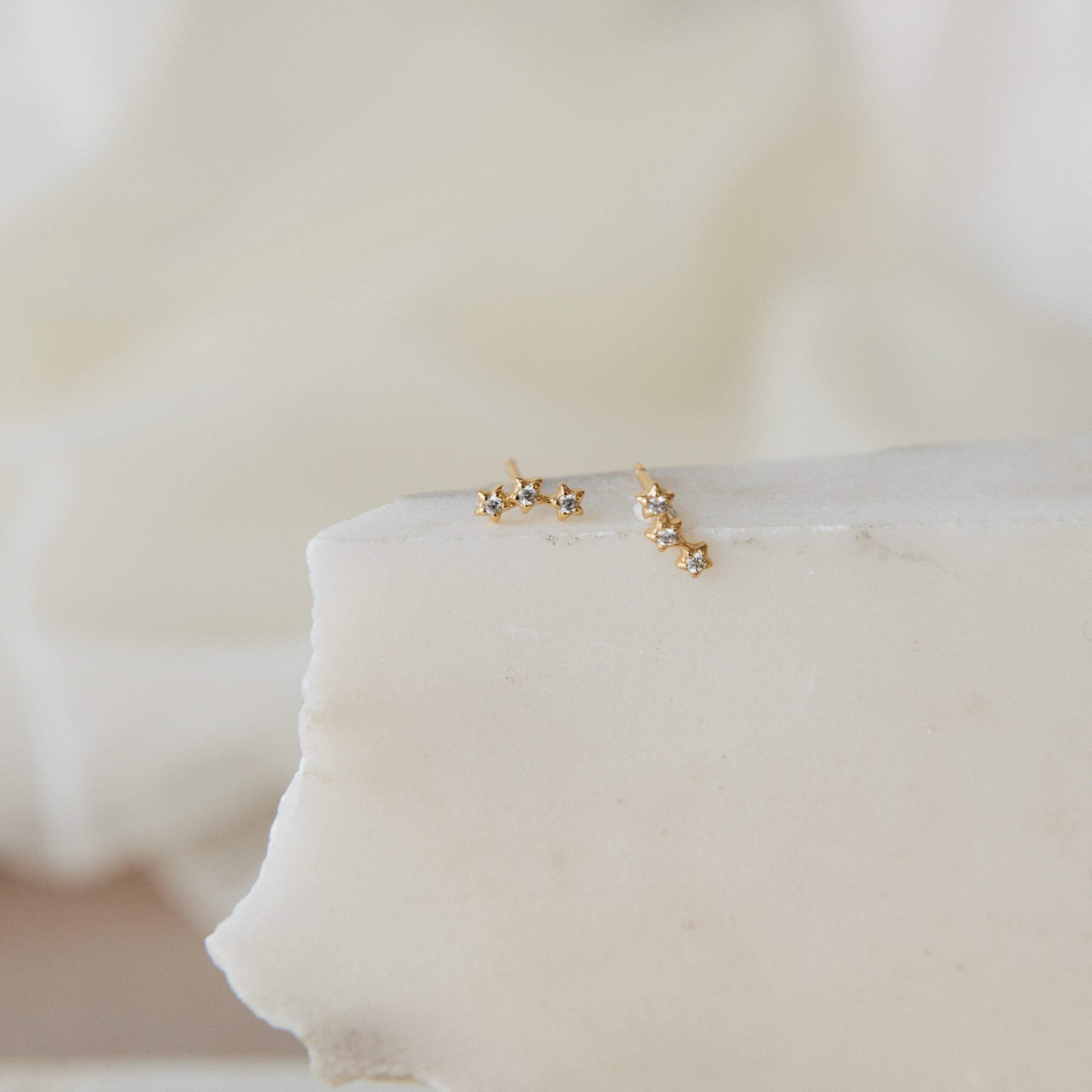 Stella Star Studs: Gold star-shaped gemstone studs, elegantly displayed on a white textured stone surface.