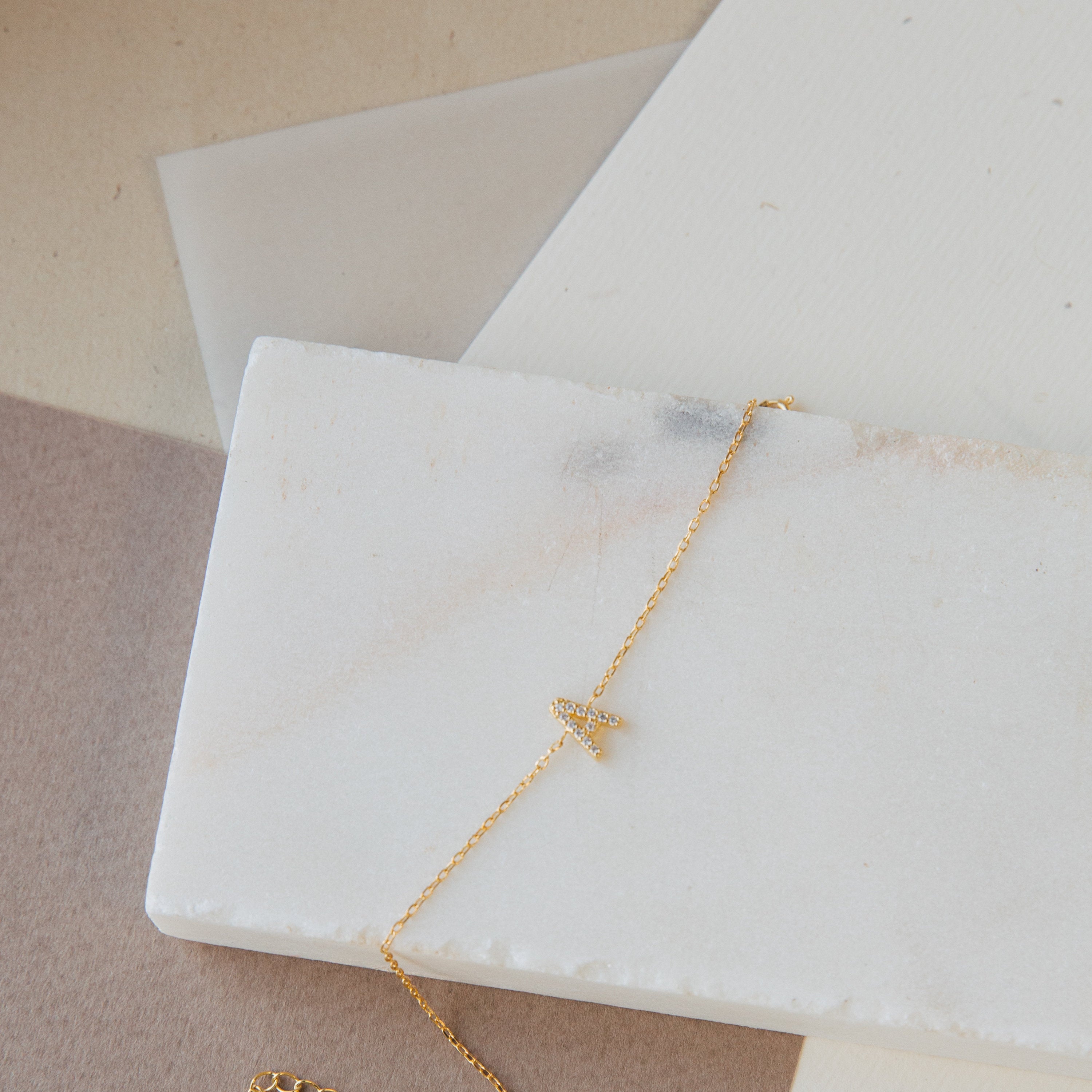 Elegant gold Pave Initial Bracelet featuring a delicate charm, showcased on a white marble slab.