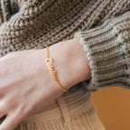 The Ladybirds Name Curb Bracelet with "Caroline" shines on a wrist, styled with a beige knit sweater—an elegant, modern bracelet perfect for any occasion.