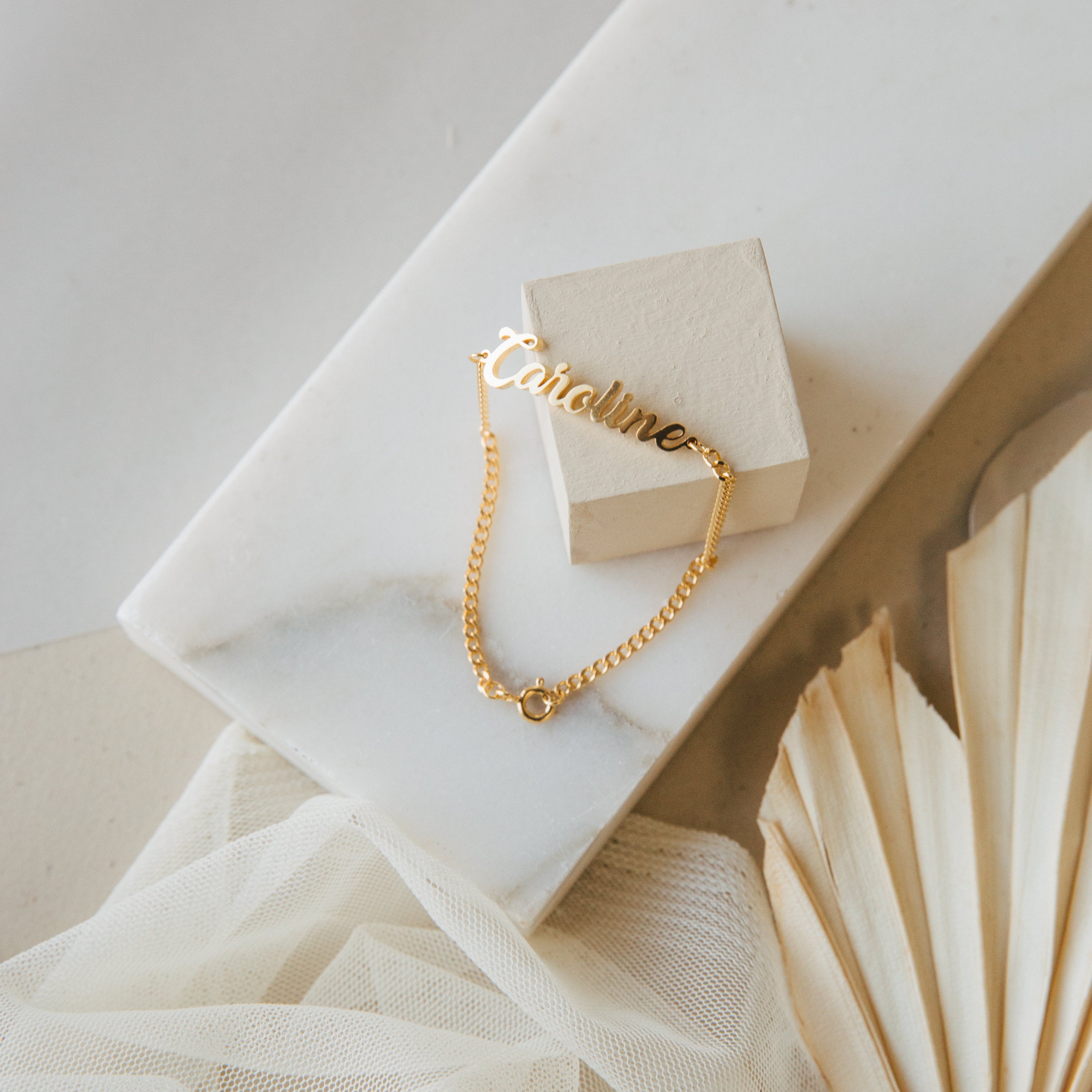 Ladybirds Name Curb Bracelet reading Caroline shown on marble and beige with neutral decor, highlighting the sleek, contemporary curb chain bracelet.