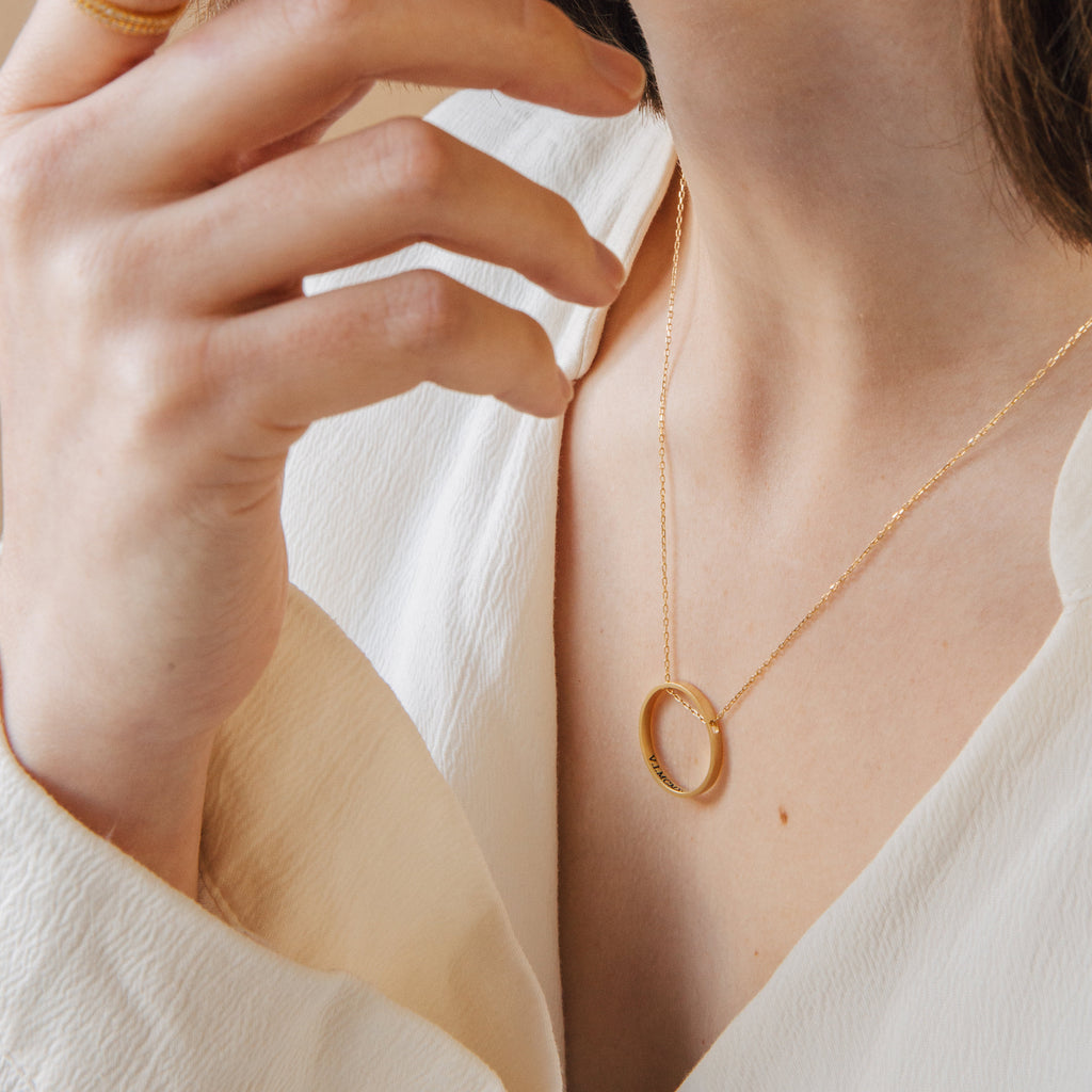 A woman in a cream blouse wears the Inner Circle Necklace in Rose Gold and a gold ring on her finger.