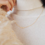 The Petite Tiny Name Necklace with a "sara" pendant, styled over a white turtleneck sweater—an elegant personalized piece and the perfect gift for mom.