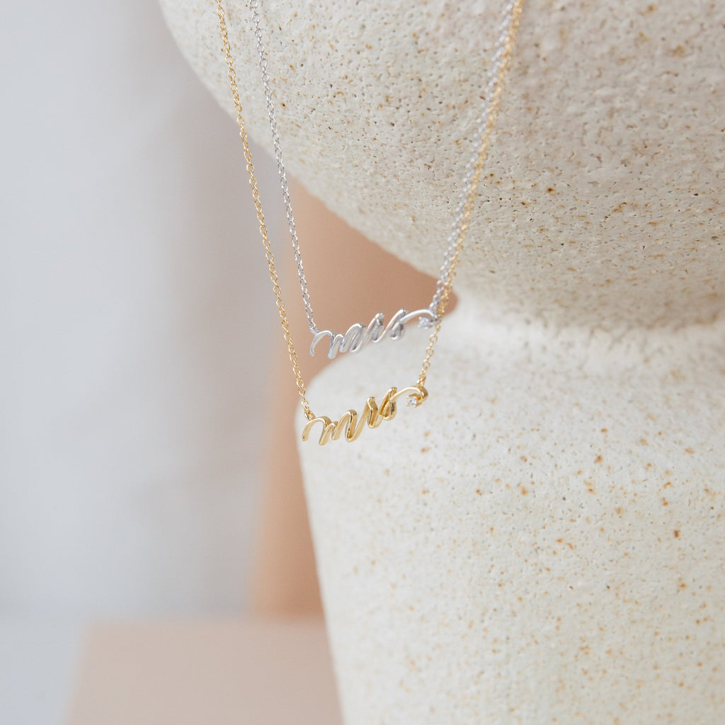 The Mrs. Necklace, available in gold and 925 sterling silver, is showcased on a textured stone surface—an ideal choice for a thoughtful wedding gift.