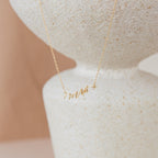 The Mrs. Necklace, featuring a script pendant, is displayed on a textured off-white ceramic vase—an elegant wedding gift idea.