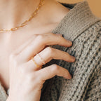 A person wearing a Paperclip Chain Ring and a gold chain necklace, paired with a chunky knitted sweater in beige tones.