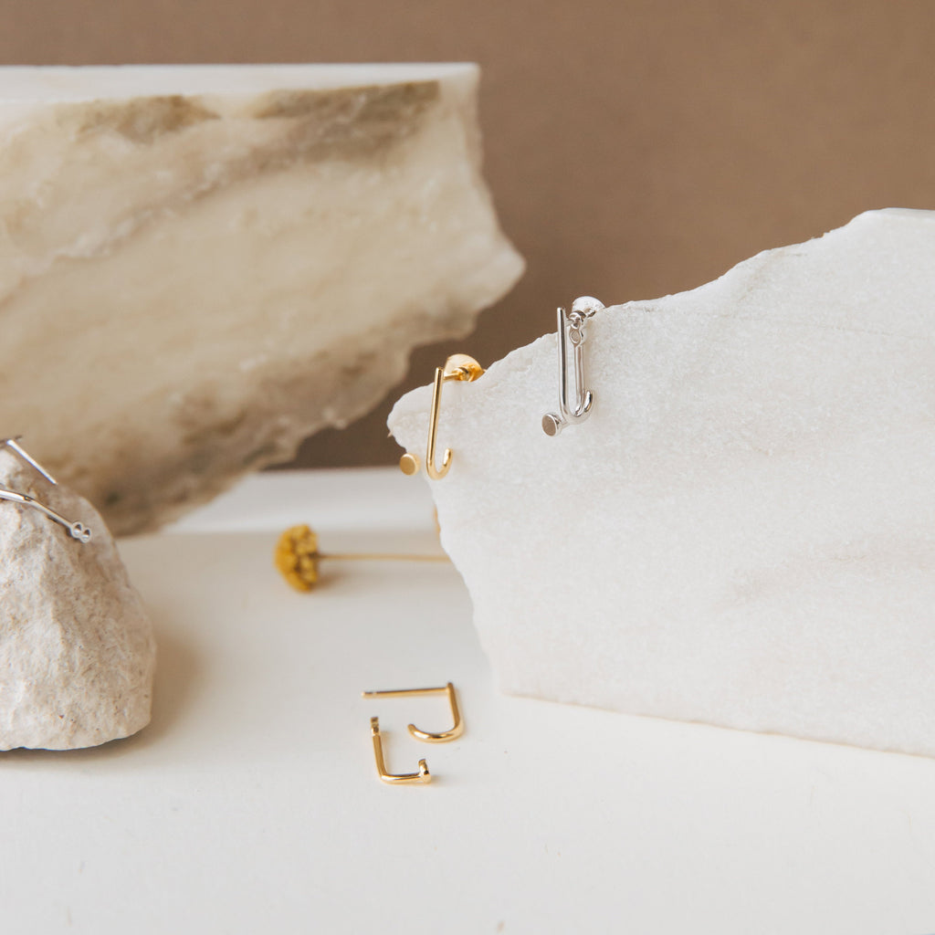 Dot Ear Jackets in minimalist gold and silver are displayed on white stone slabs with a neutral background—ideal modern earrings for contemporary style lovers.