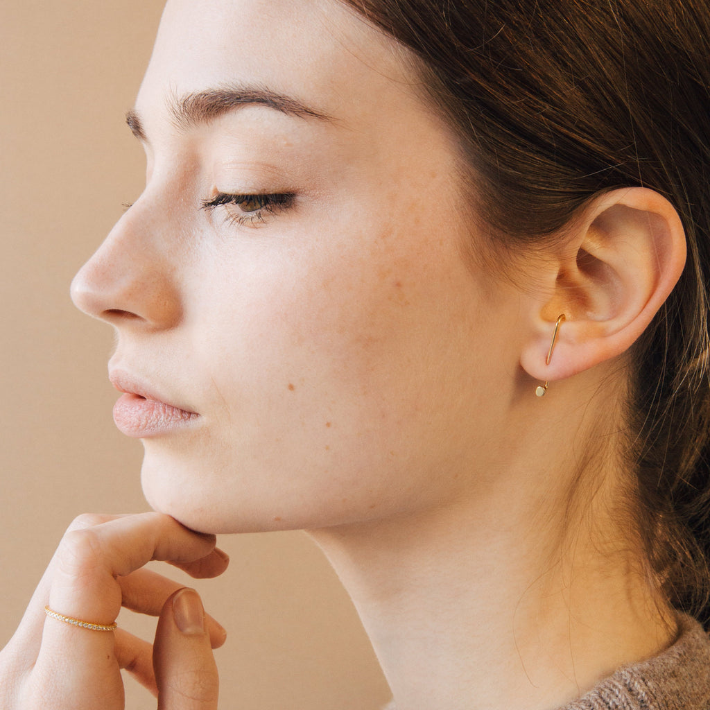 A woman in profile with closed eyes touches her chin gently, wearing gold Dot Ear Jackets and a gold ring.