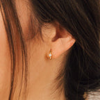 Close-up of a woman's ear adorned with Athena Huggies—gold hoop earrings set with a single diamond-shaped stone.