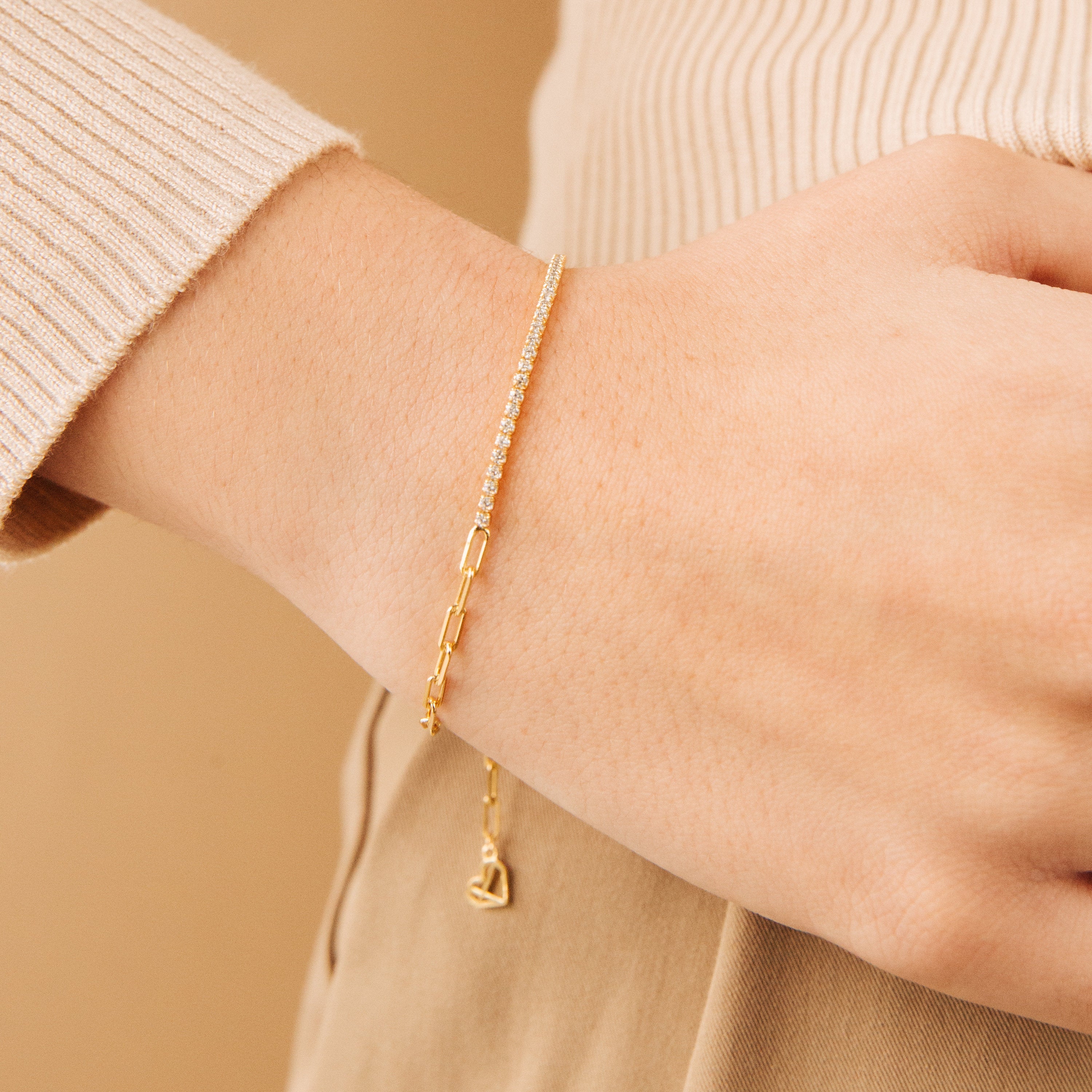 The Klara Tennis Bracelet shines on a wrist alongside a beige long-sleeve top—ideal for those who appreciate minimalist jewelry.