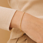 A close-up of a wrist wearing the Klara Tennis Bracelet alongside a gold chain bracelet, styled with a beige outfit for an elegant minimalist jewelry look.