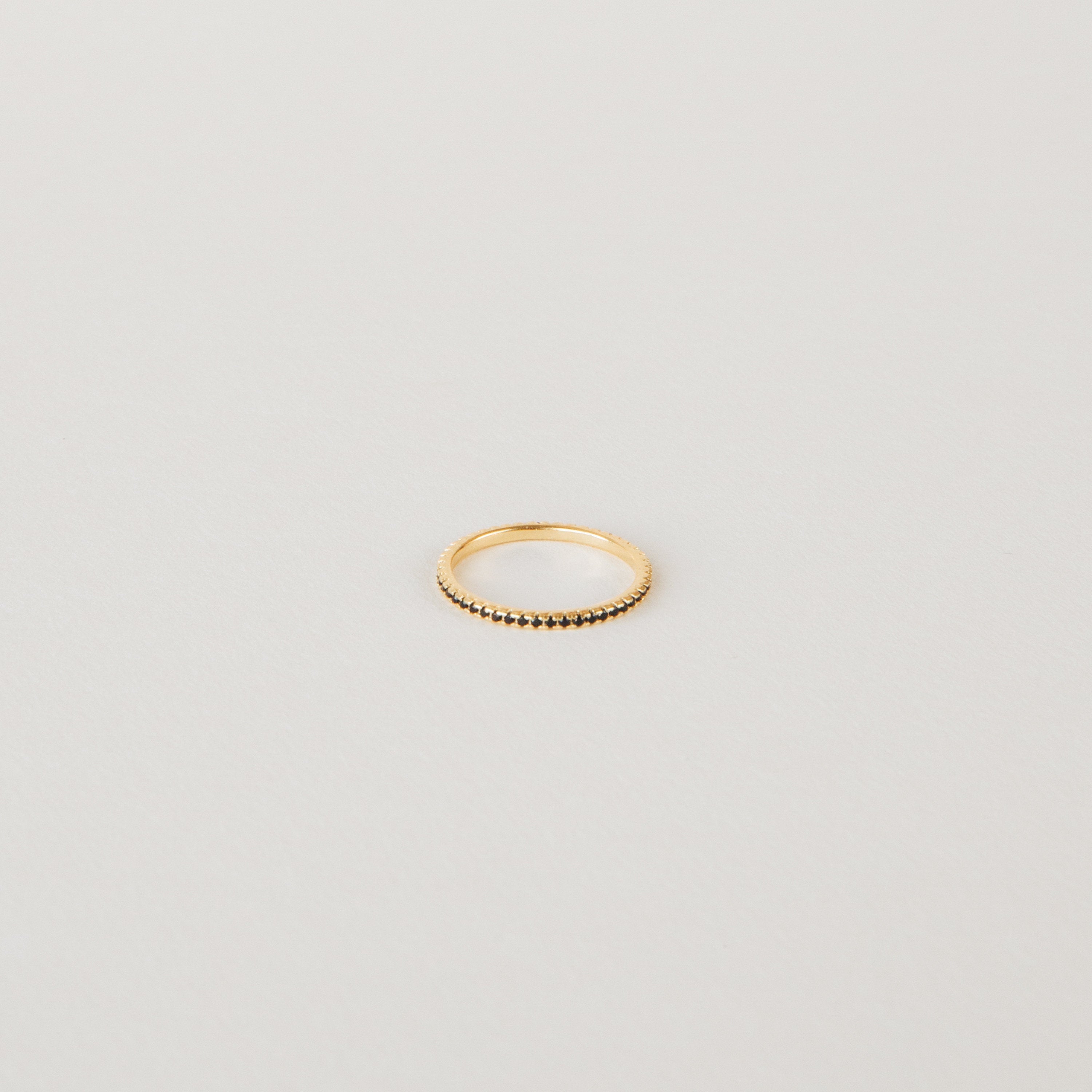 The Amber Eternity Ring is a delicate gold, stackable ring featuring small beads along its band, shown on a plain white background.