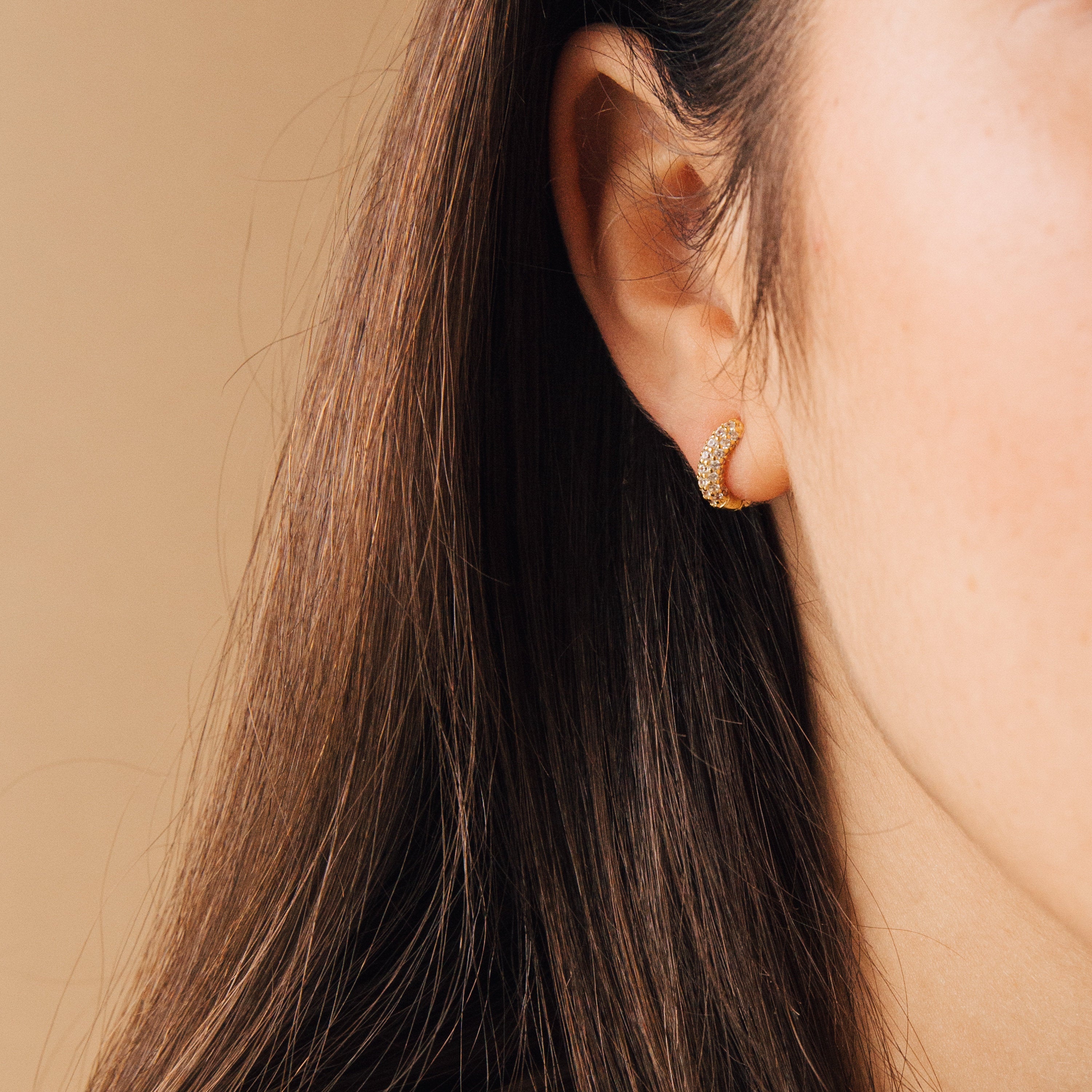 Close-up of a woman with long brown hair wearing Kira Pave Huggies, the diamond hoops sparkling as they catch the light.