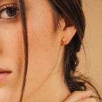 Close-up of a woman wearing the Enya Huggies, small gold earrings featuring a star-shaped prong design.