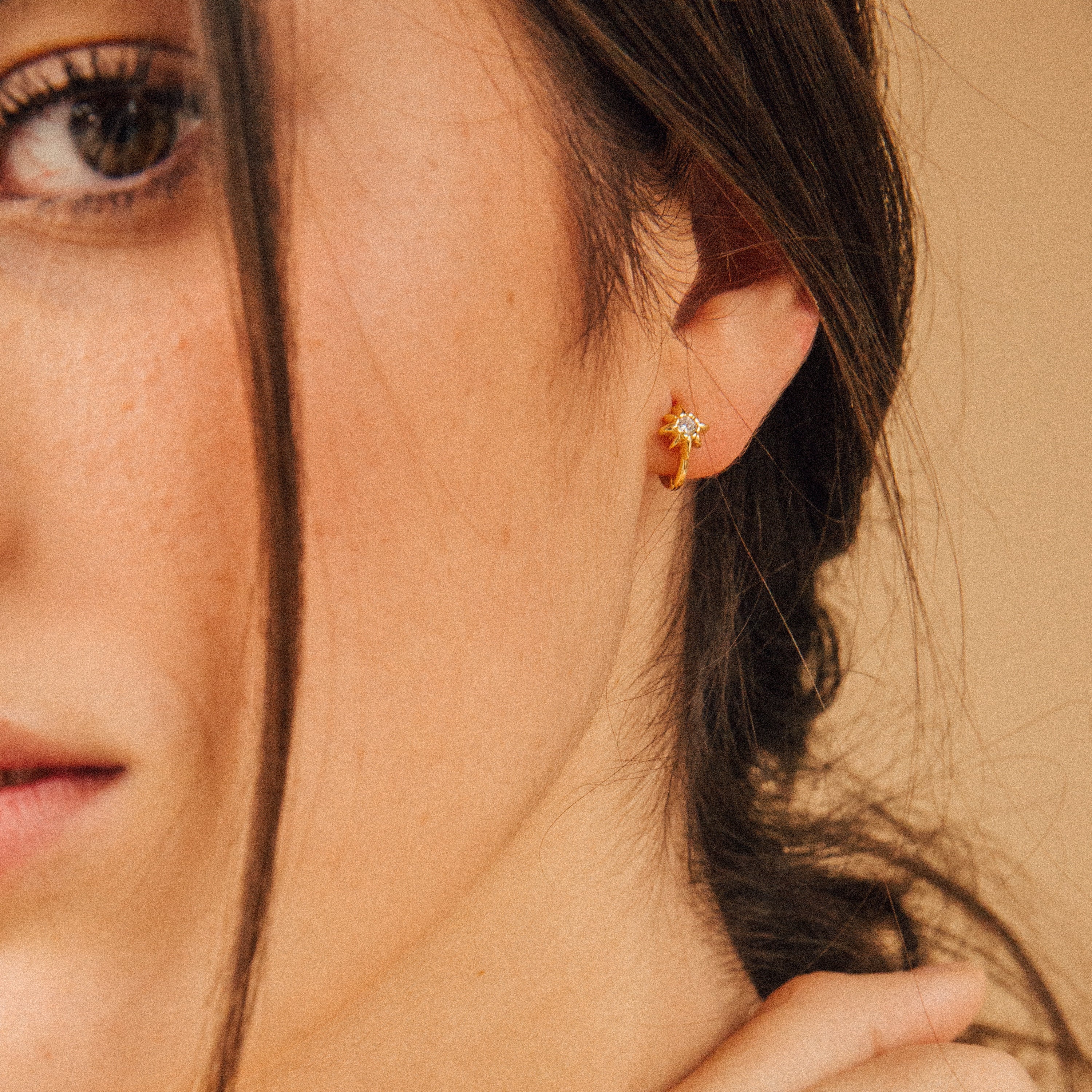 Close-up of a woman wearing the Enya Huggies, small gold earrings featuring a star-shaped prong design.