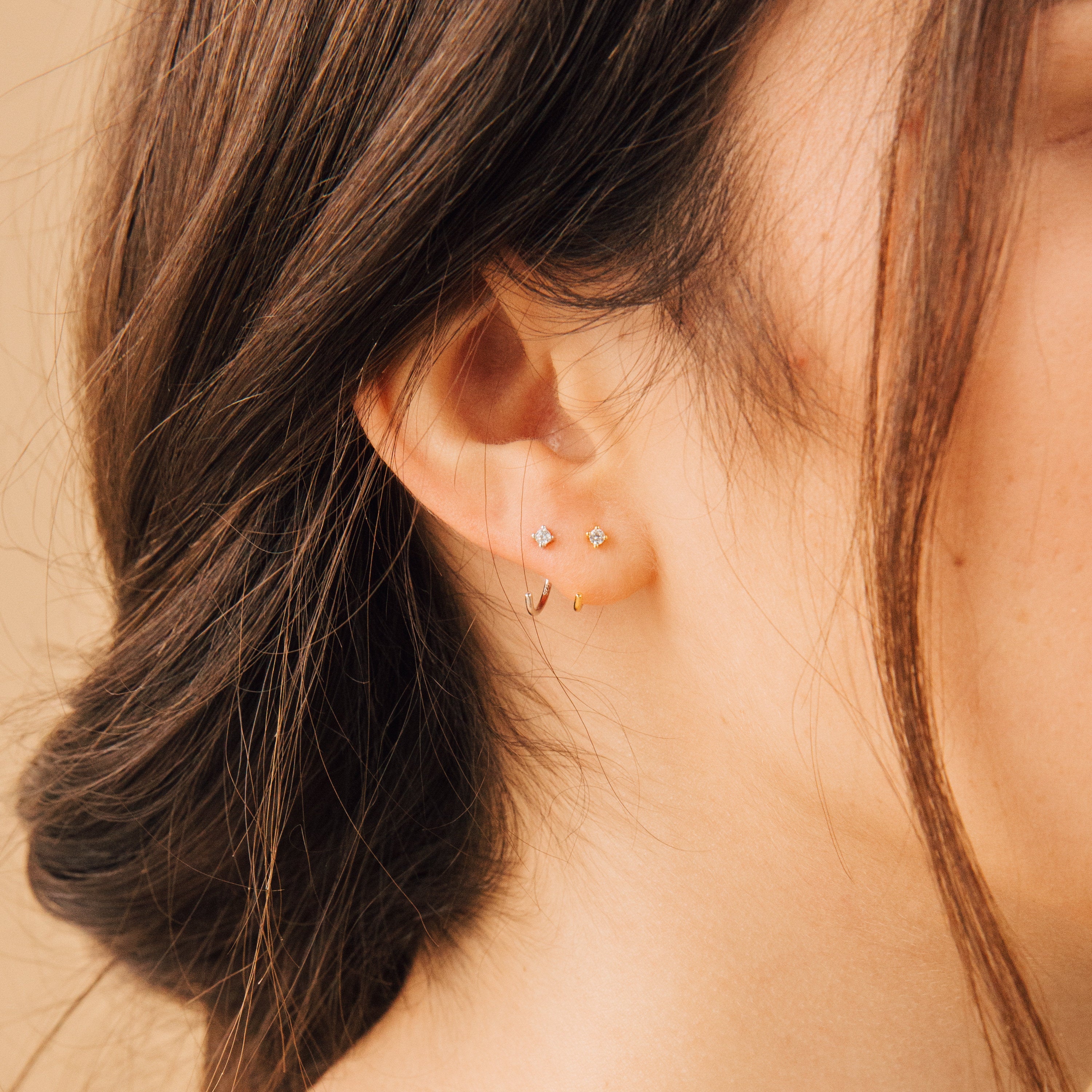 Close-up of a woman's ear featuring the Saylor Huggies alongside two small studs, with her hair loosely tied back.