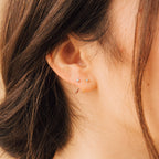 Close-up of a woman's ear adorned with two small studs and the Saylor Huggies, showcasing a graceful mix of delicate earrings.