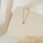 Rae Diamond Necklace with solitaire diamond pendant on 18K gold chain on cream background.