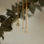 Three gold necklaces with jeweled letter pendants A, R, and T hang before blurred green foliage—a perfect Dangling Pave Initial Necklace and a thoughtful gift for women who love delicate jewelry.