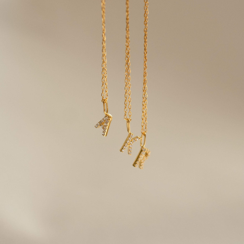 Three delicate necklaces with sparkling pave initial K pendants hang against a light, neutral background—a stylish Dangling Pave Initial Necklace, perfect as a thoughtful gift for women.