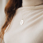 A woman in a beige turtleneck wears an Oval Fingerprint Necklace featuring personalized etching that reads "love Mom," highlighting elegant memorial jewelry.