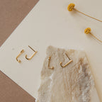 Two pairs of Dot Ear Jackets are displayed on textured paper with two yellow dried flowers nearby, highlighting the modern earrings' minimalist geometric style.