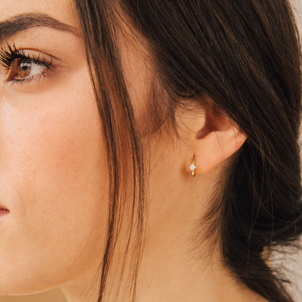 Close-up of a woman's face and ear wearing the Athena Huggies, a small gold earring shaped like a star.