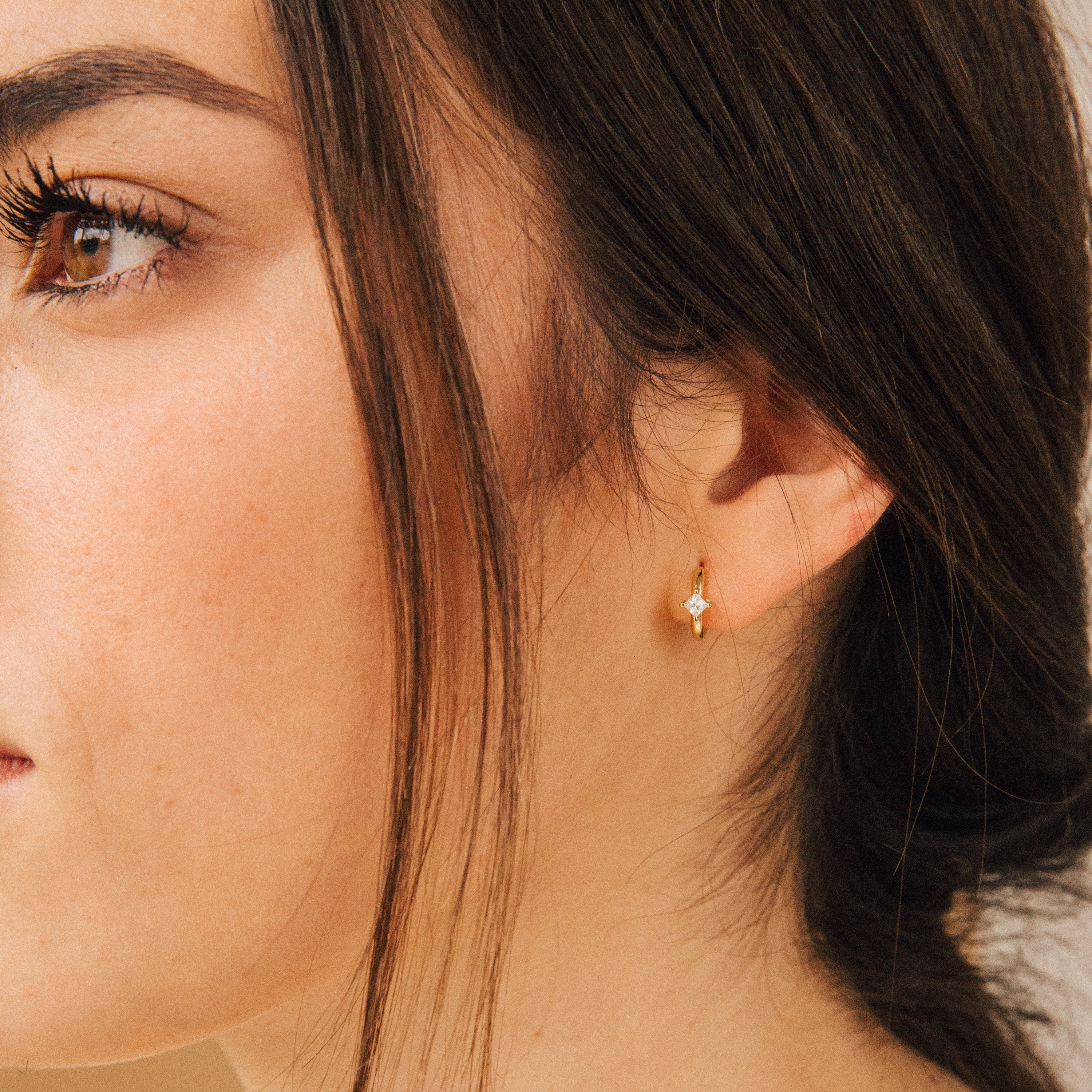 Close-up of a woman's face and ear wearing the Athena Huggies, a small gold earring shaped like a star.