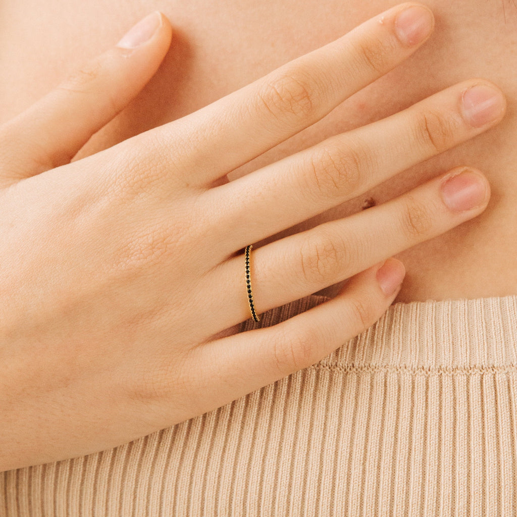 A hand adorned with the Amber Eternity Ring, a delicate gold stackable piece, rests on beige ribbed fabric.