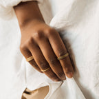 A hand adorned with gold rings, featuring the Amber Eternity Ring, rests gracefully on white fabric.
