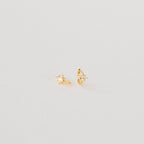 The Enya Huggies are small gold earrings, each with a star-shaped prong design and an iridescent diamond at the center.