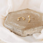 The Saylor Huggies, gold nose rings with small diamonds and dainty hoop earrings, are displayed on a hexagonal stone tile against a cream fabric background.