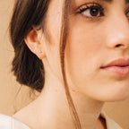 Close-up of a woman with brown hair in a low bun, wearing natural makeup and the Saylor Huggies.