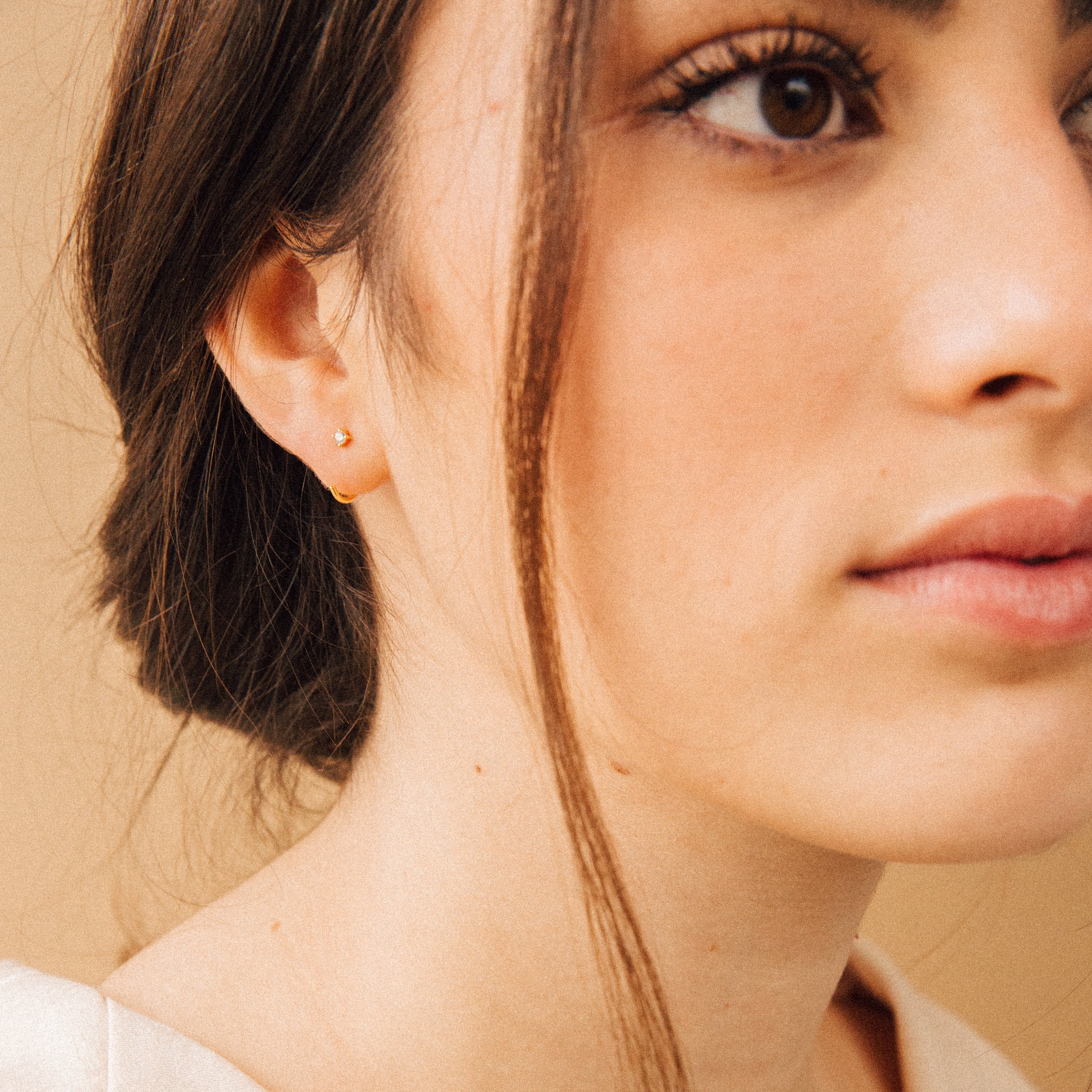 Close-up of a woman with brown hair in a low bun, wearing natural makeup and the Saylor Huggies.